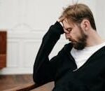 A man sits pensively with his hand on his face, capturing a moment of introspection and stress.